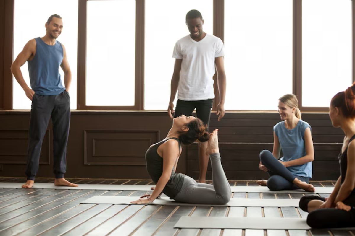 A group of people observing a yoga class, focusing on a practitioner demonstrating a pose on a mat in a spacious studio.
