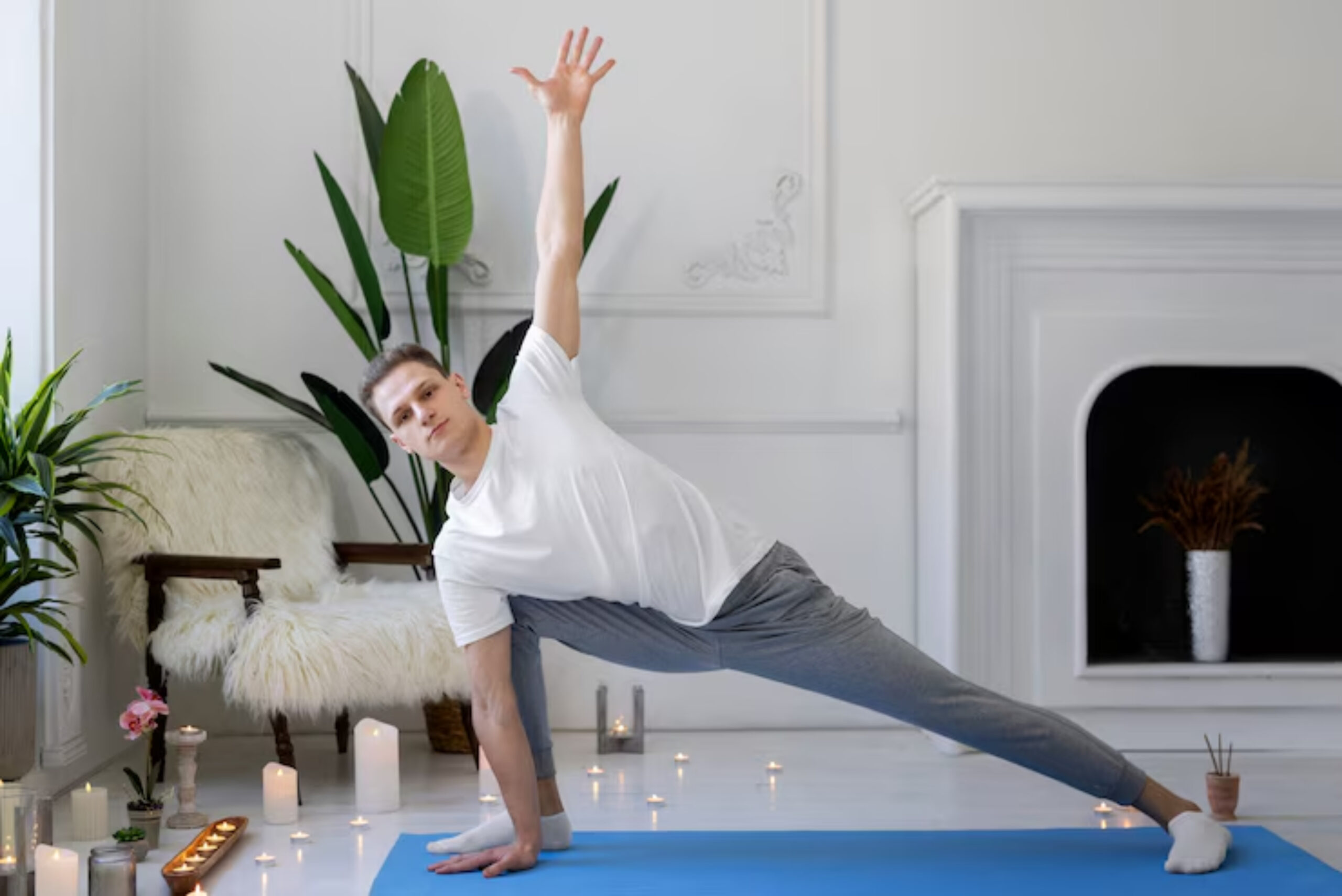  A person performs a yoga pose on a blue mat in a serene, bright room adorned with plants and candles.