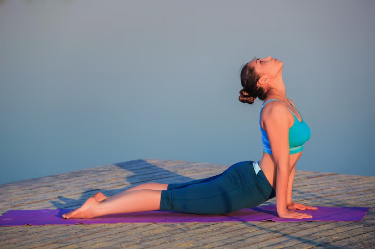 A person performs the Cobra pose on a yoga mat by the water, surrounded by a serene, calming atmosphere.