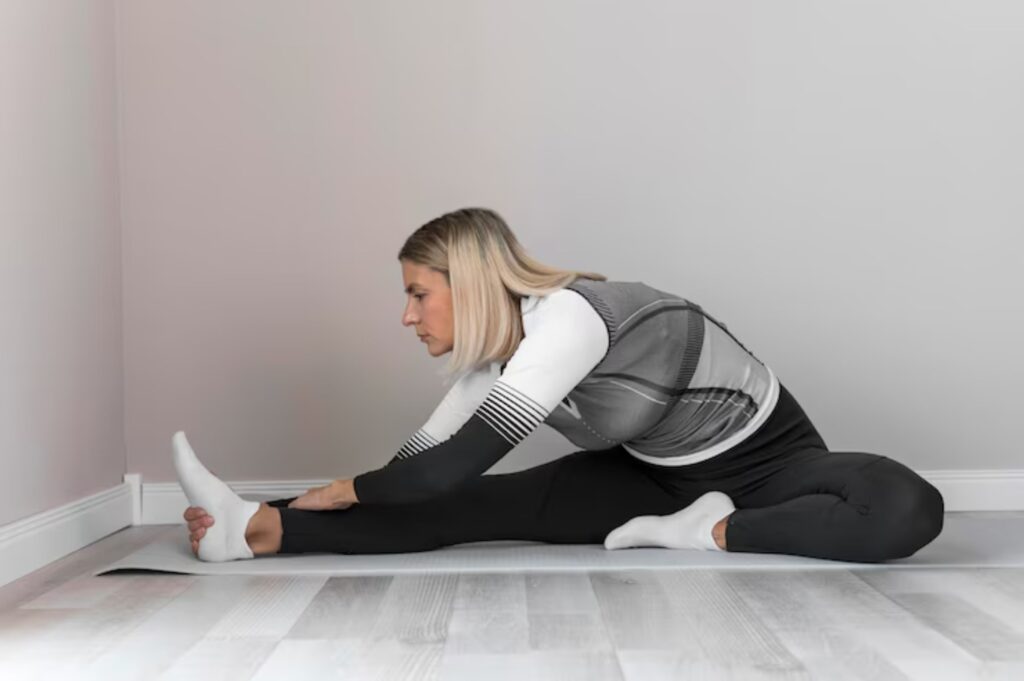 A person stretches on a yoga mat in a minimalist room with light gray walls and wooden flooring, focusing on flexibility and wellness.