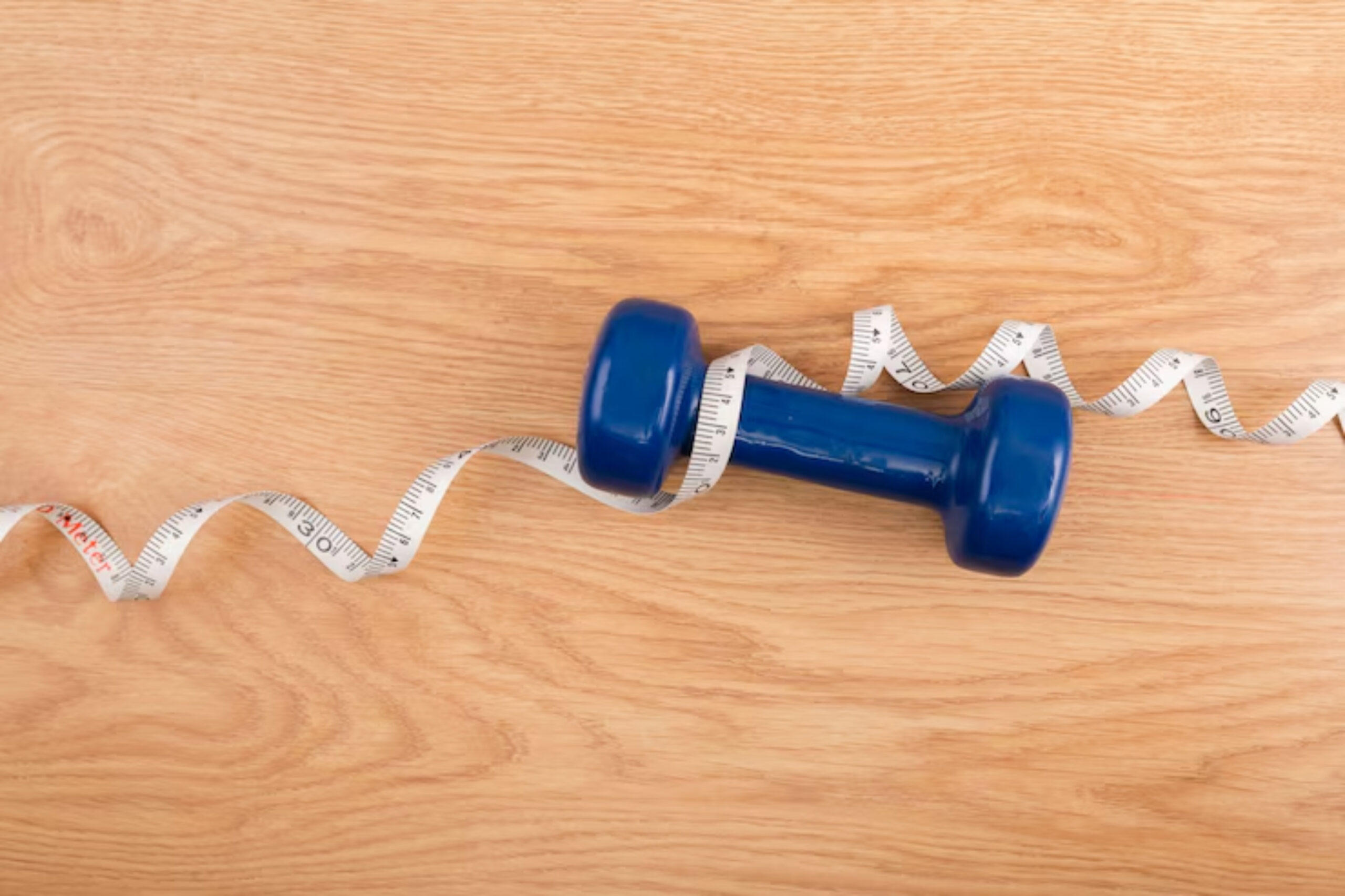 A blue dumbbell rests on a wooden surface, entwined with a measuring tape, symbolizing fitness and health. 