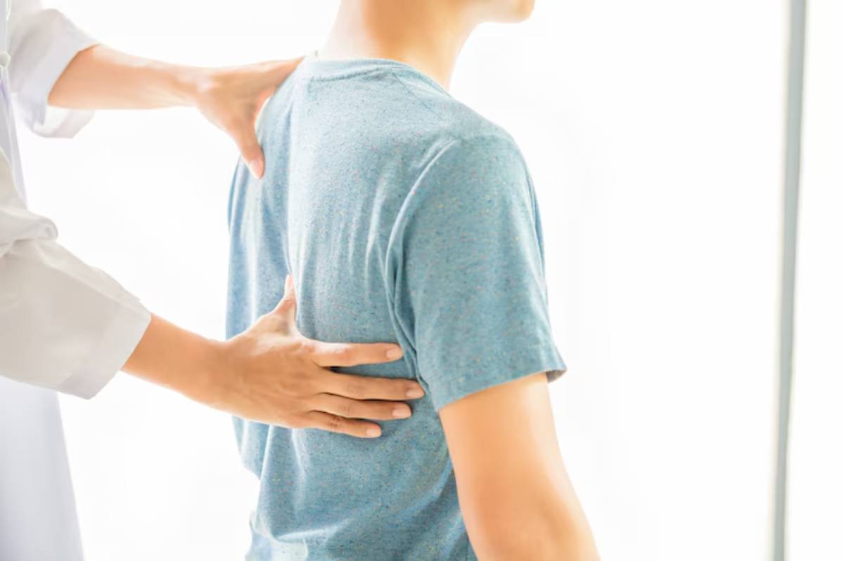  A healthcare professional's hand gently touches a patient's back for assessment in a bright, clinical setting.