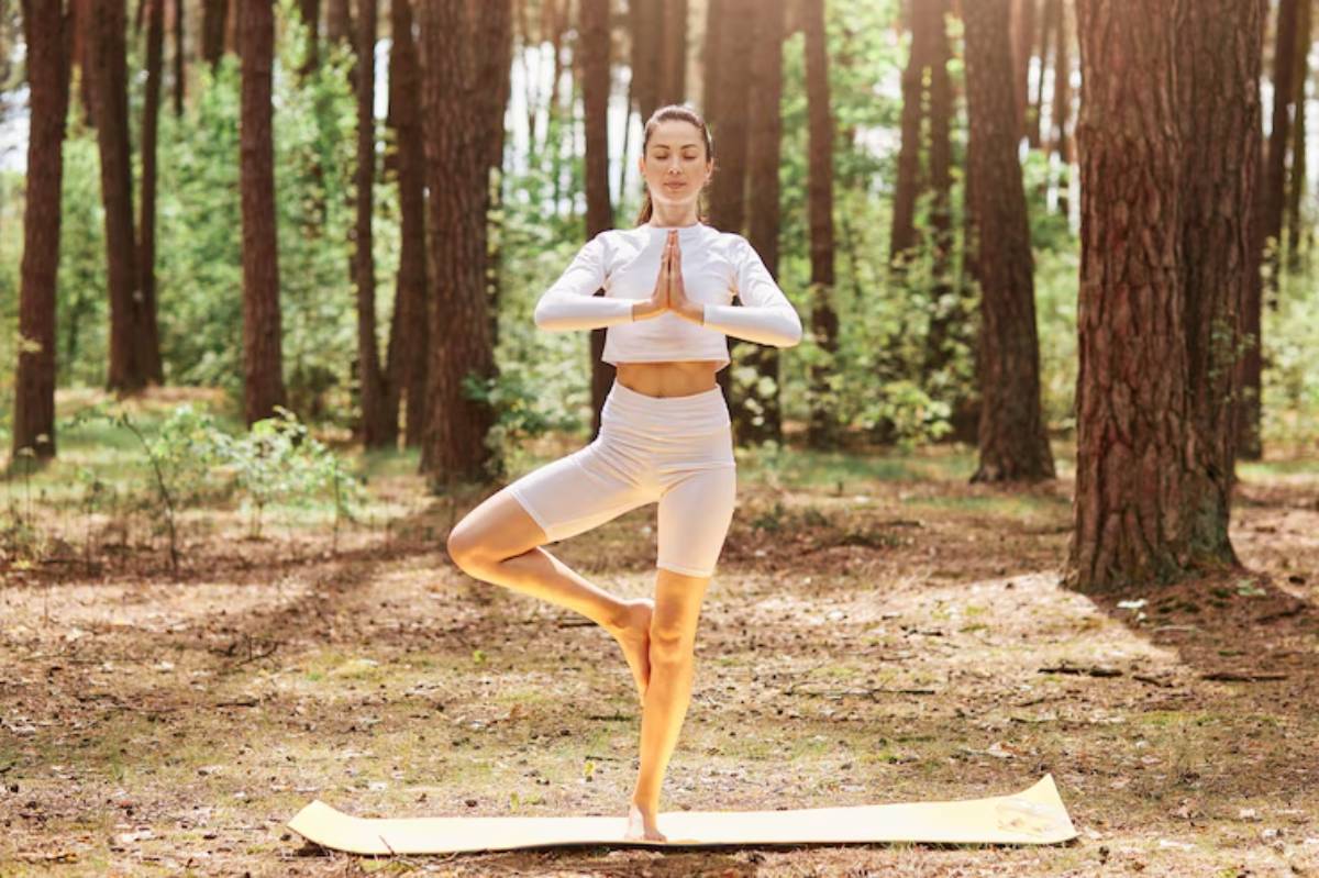  A person practicing yoga outdoors in a forest, balancing on one leg with hands in a prayer position, bathed in soft sunlight.