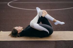 A person in athletic wear performs a yoga pose on a mat on an outdoor court surface. The scene conveys relaxation and focus.