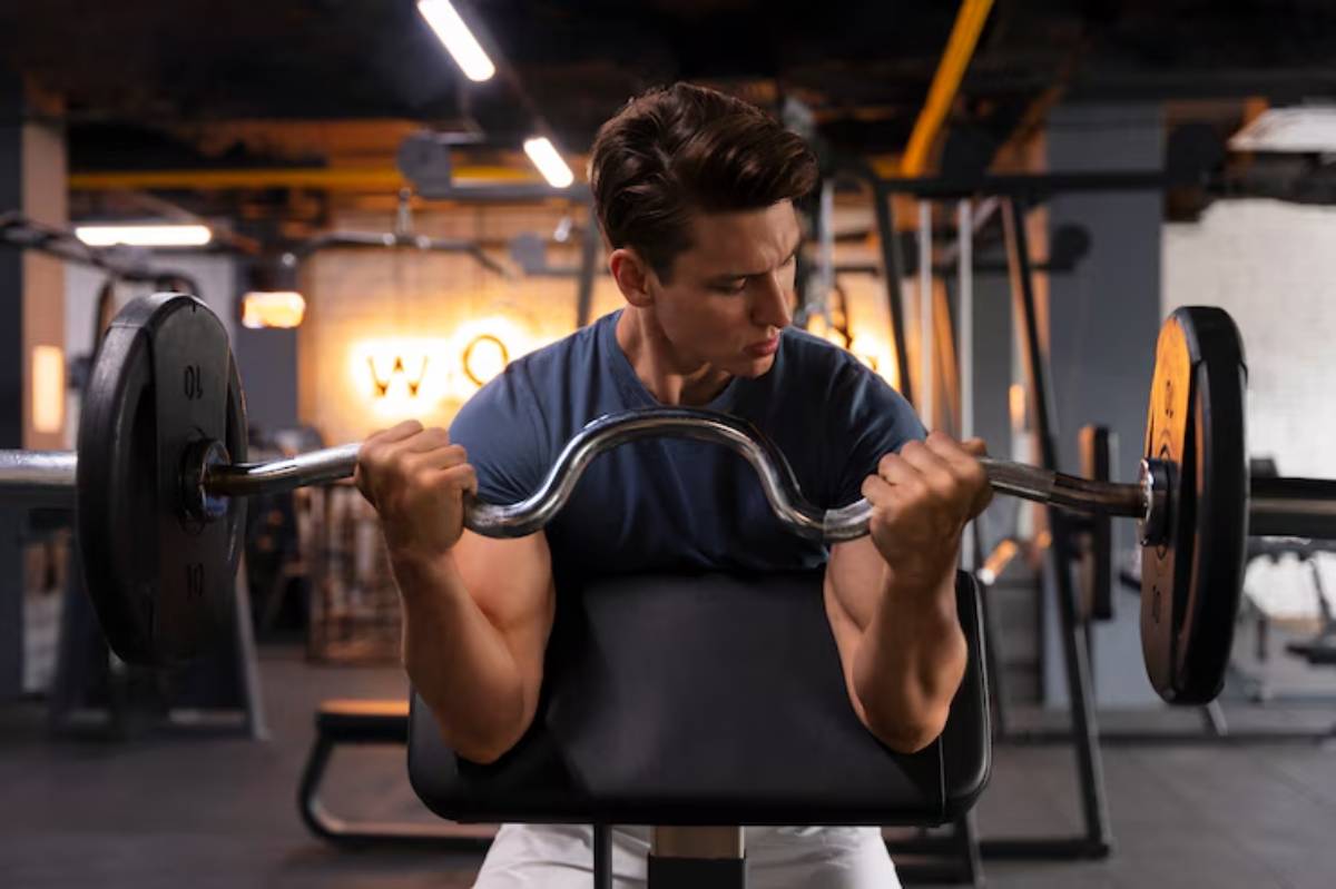 A person is lifting a barbell in a gym, showcasing strong arm muscles. The background features gym equipment and ambient lighting.